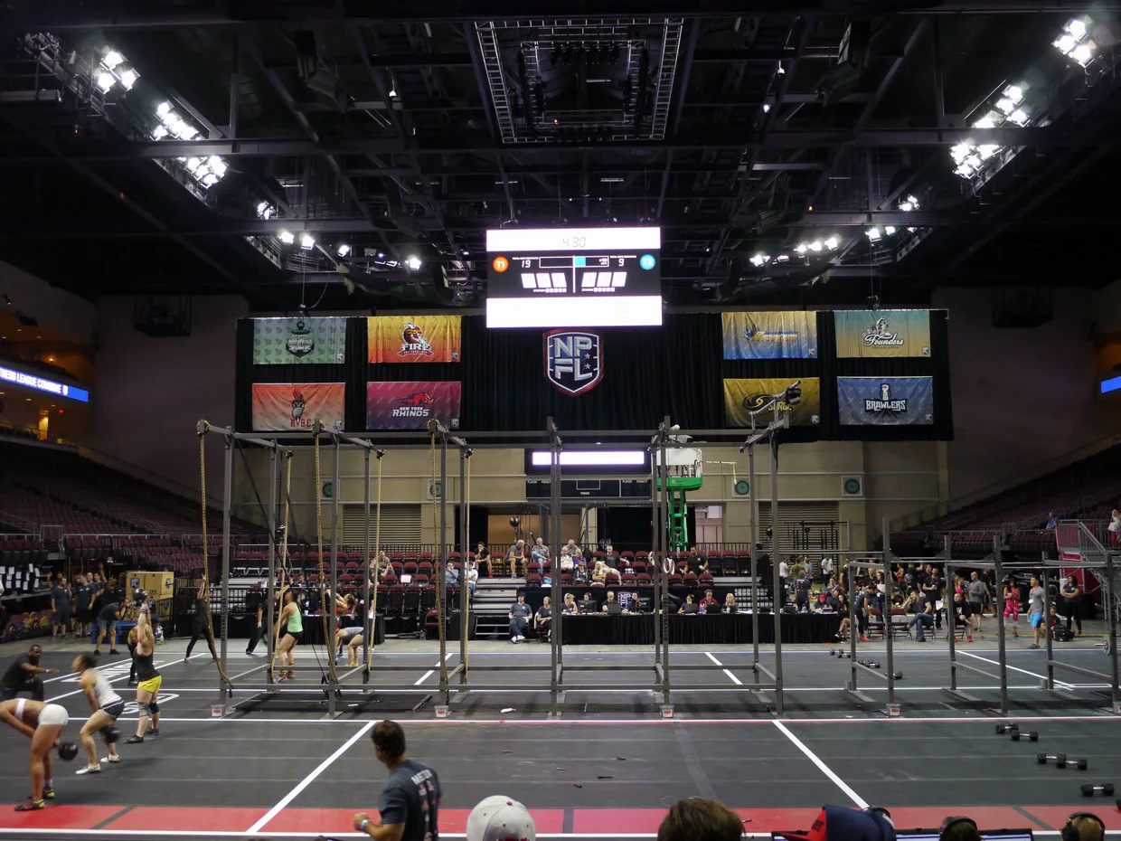 An NPGL match in an arena — athletes on the grid floor beneath the overhead scoreboard and team banners